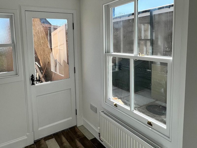 Wooden sash window and doors. Frames are painted on white like rest of the room.
